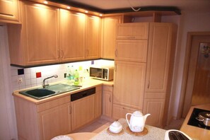 A kitchen with wooden cabinets, a microwave, a sink, and a stove. - Alice's Holiday Apartment 1 (Arnstadt)