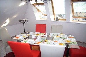A dining area with a glass table, red and white chairs, and a chandelier. - Alice's Holiday Apartment 1 (Arnstadt)