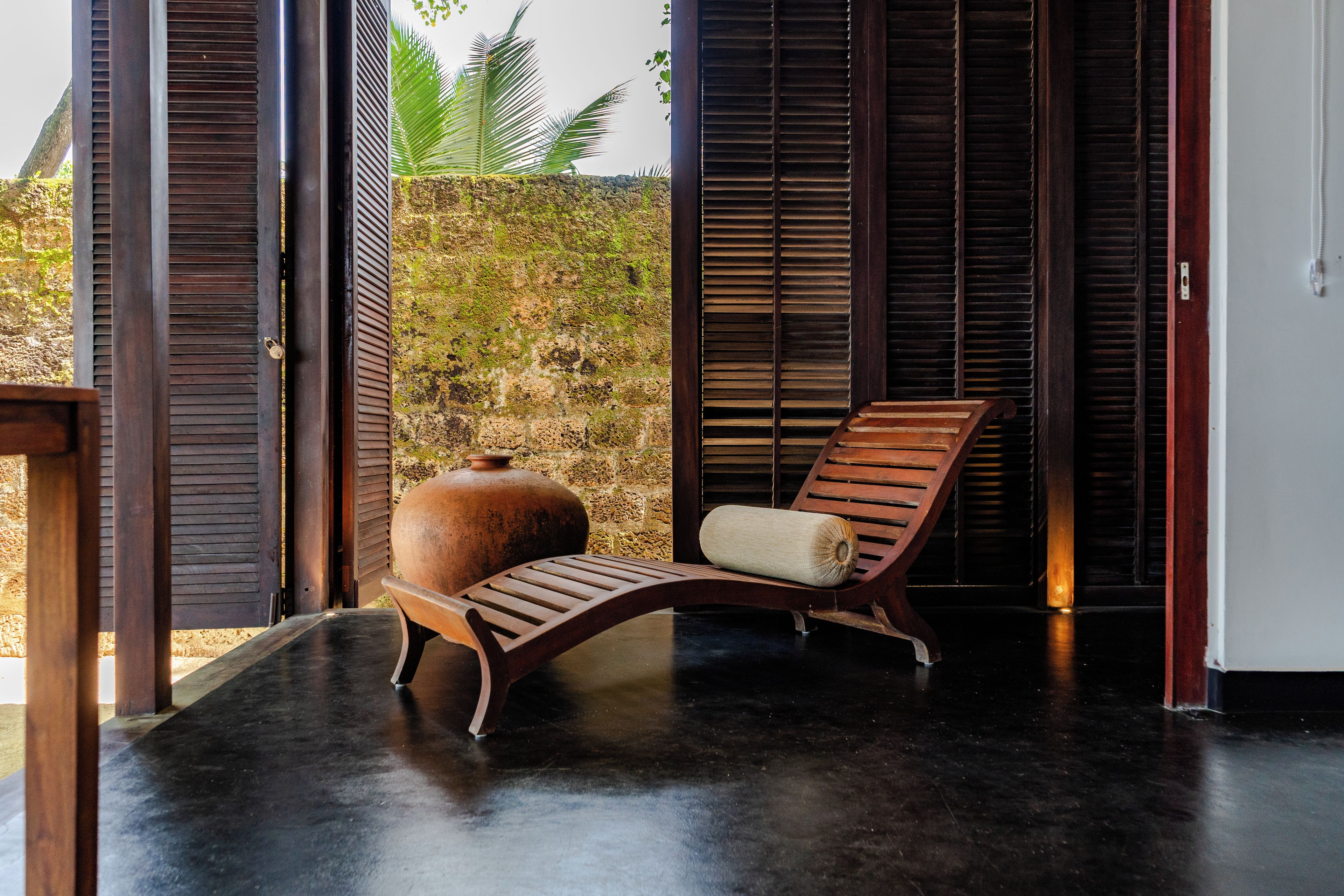 A room with a wooden chair, a large pot, and a view of a natural landscape.