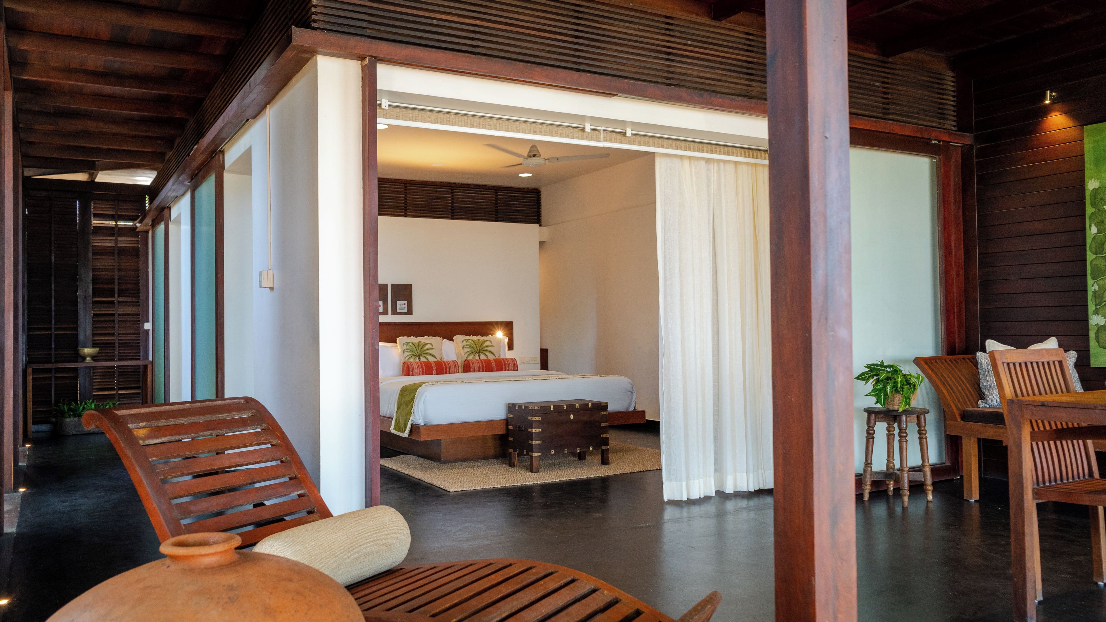 Habitación de hotel con una cama, una silla de madera, una mesita pequeña y una planta en maceta.