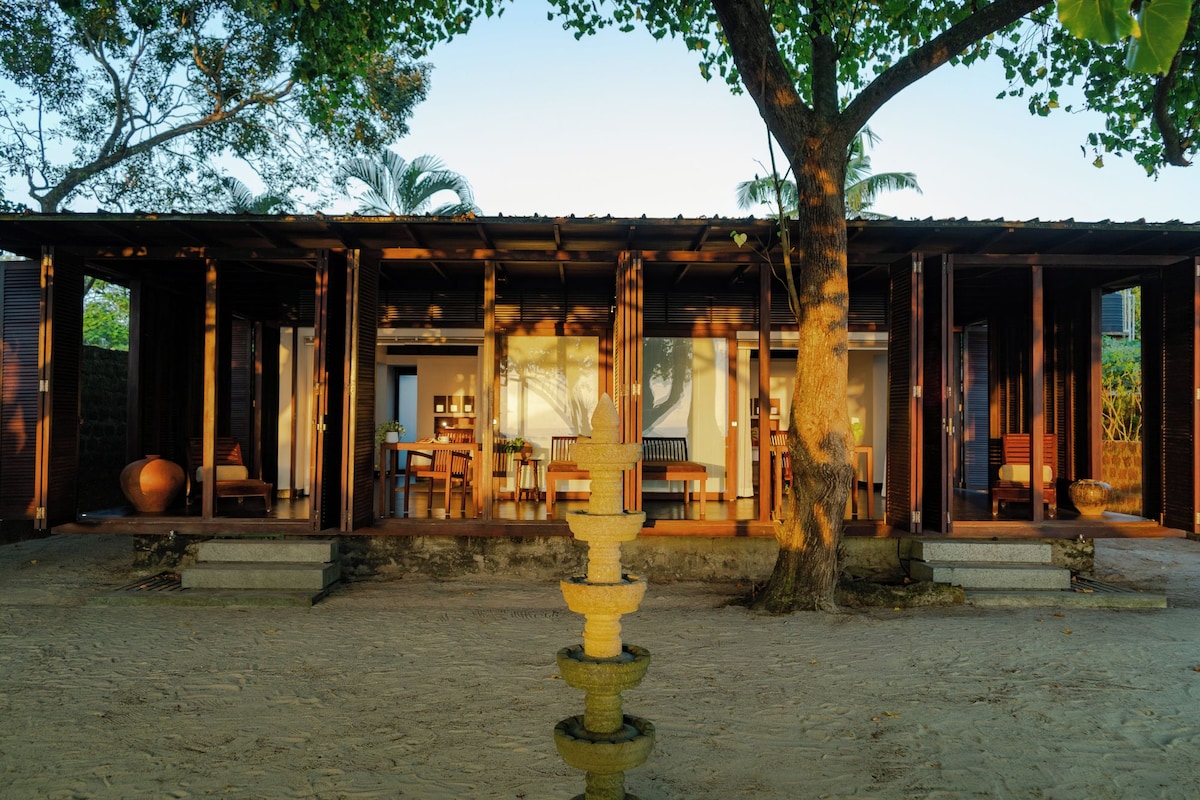 A traditional wooden building with an open veranda, a stone water feature in the foreground, and a view of the interior through the open doors.