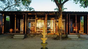 A traditional wooden building with an open veranda, a stone water feature in the foreground, and a view of the interior through the open doors.