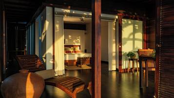 A room with a bed, a wooden chair, a table, and a potted plant.