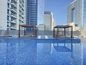 Ein Schwimmbad mit zwei hölzernen Pavillons, umgeben von Hochhäusern.