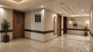A hotel lobby with a marble floor, wooden door, directional signs, and potted plants.