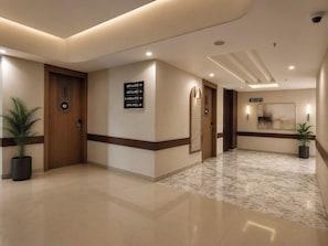 Un hall d’hôtel avec un sol en marbre, une porte en bois, des panneaux indicateurs et des plantes en pot.