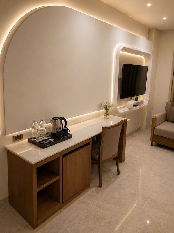 Une chambre d’hôtel moderne avec une console blanche, un téléviseur fixé au mur, un meuble en bois et un canapé beige.