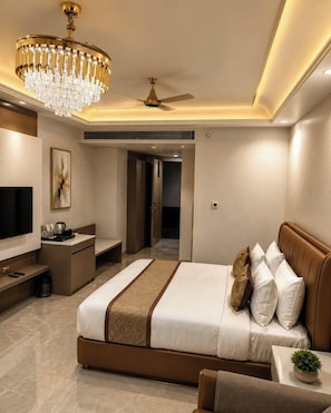 A modern hotel room with a large bed, a television, a desk, and a chandelier. - Royal Damyanti Palace (damoh)