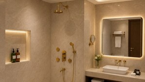 Et moderne badeværelse med badekar, bruser med guldfarvede armaturer, et spejl med underskab og en hylde med toiletartikler.
