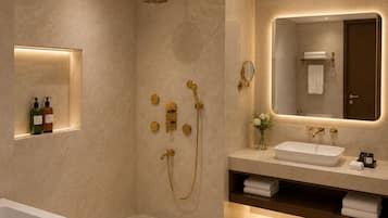 A modern bathroom with a bathtub, a shower with gold fixtures, a vanity with a mirror, and a shelf with toiletries.