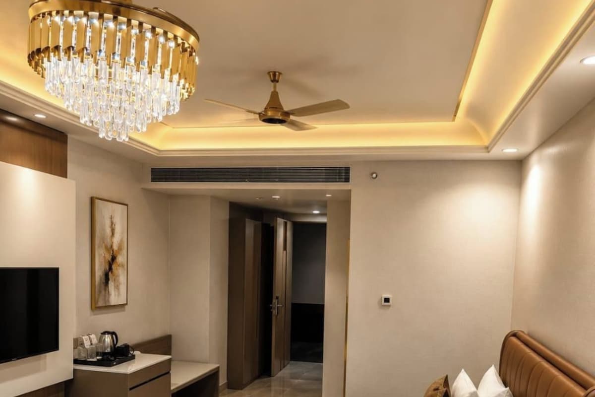 A modern hotel room with a large bed, a television, a desk, and a chandelier.