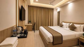 A hotel room with a bed, bedside table, TV, curtains, and a ceiling fan.