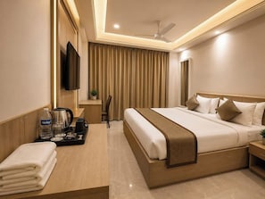 A hotel room with a bed, bedside table, TV, curtains, and a ceiling fan. - Royal Damyanti Palace (damoh)