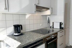 A modern kitchen with white cabinets, a granite countertop, a built-in oven, and a coffee maker. - Holiday apartment with 1 bedroom (Lindau)
