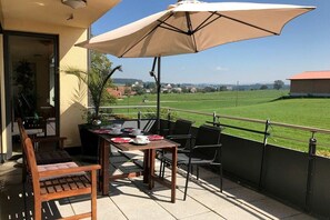 An outdoor patio with a table and chairs, a large umbrella, and a view of a green field. - Holiday apartment with 1 bedroom (Kressbronn)