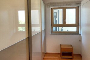 A small room with a window, a wooden floor, and a small wooden stool. - Holiday apartment with 1 bedroom (Kressbronn)