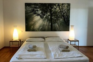 A double bed with two side tables, each with a lamp, and a large forest-themed painting above the bed. - Holiday apartment with 1 bedroom (Kressbronn)