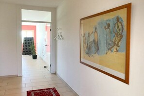 Passadís amb una obra d'art emmarcada, una catifa vermella amb dibuixos i una porta que condueix a una altra habitació.