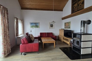 Ein Wohnzimmer mit einem roten Sofa, einem Holztisch, einem Fernseher und einem schwarz-weißen Herd.