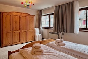 A hotel room with two beds, a wooden wardrobe, a window with curtains, and a ceiling light fixture. - Holiday apartment with 1 bedroom (Langenargen)