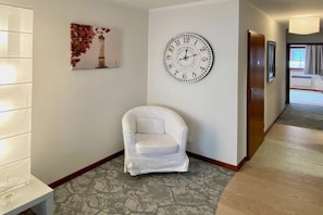 A hotel hallway with a white armchair, a wall clock, and a framed picture of a lighthouse. - Holiday apartment with 1 bedroom (Langenargen)