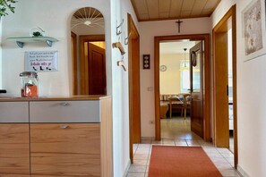 A hallway with a wooden door leading to a dining area, a glass shelf with a plant, and a sign with text. - Uschi's Summer Garden (Wangen im Allgäu)