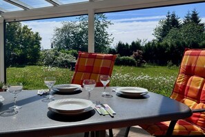 An outdoor dining area with a table set for two, surrounded by chairs with plaid cushions, and a view of a garden with trees and grass. - Uschi's Summer Garden (Wangen im Allgäu)