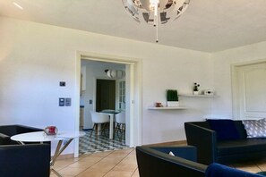 Een moderne woonkamer met een bank, een eettafel en een keuken die zichtbaar is door een open deur.