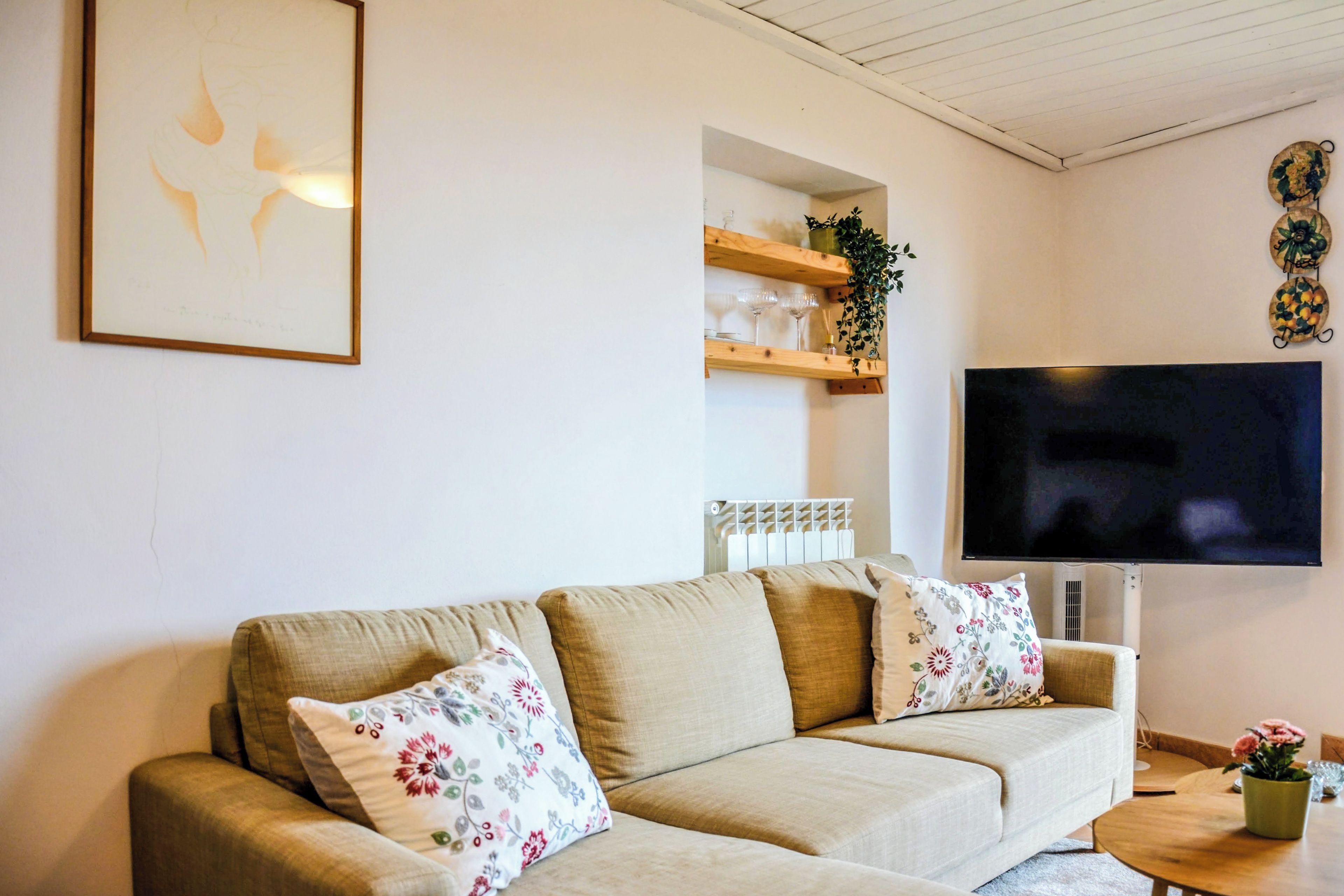 A living room with a sofa, a flat-screen TV, and a wall-mounted shelf with decorative items.