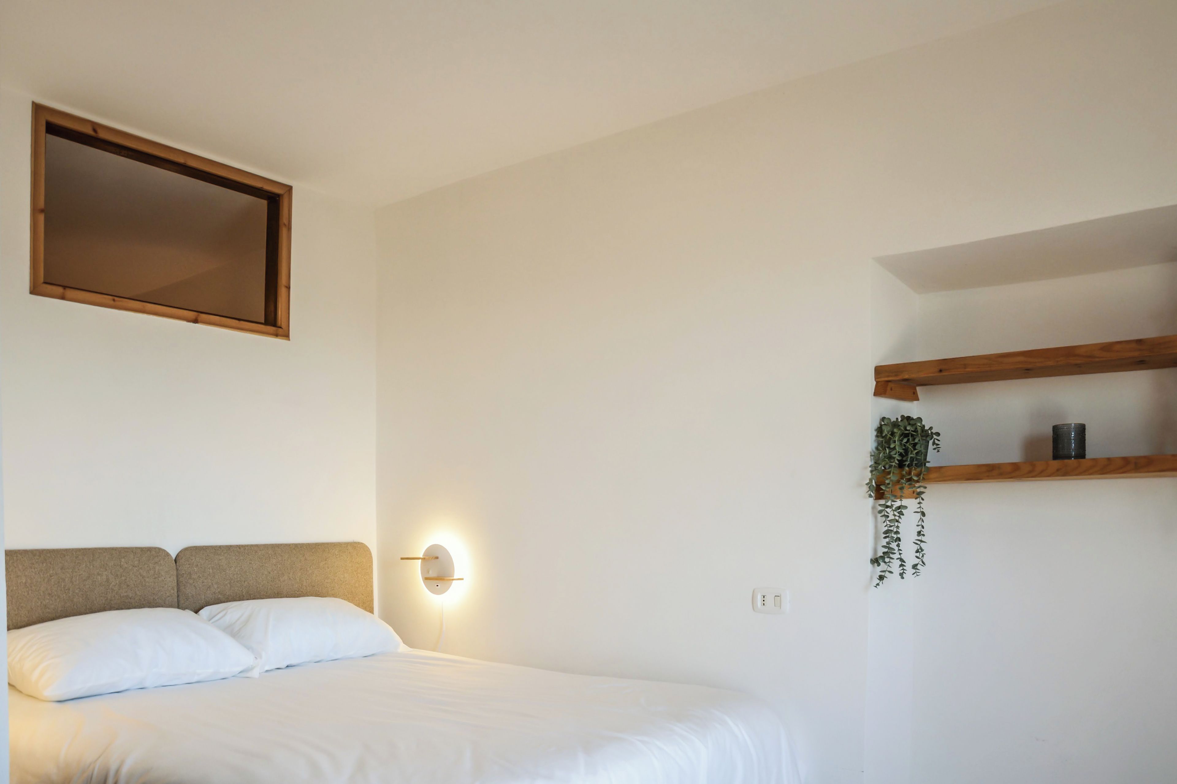 Un dormitorio con cama, luz empotrada, espejo y estante con una planta.