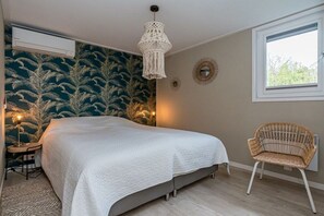 Ein Schlafzimmer mit einem Bett, einem Sessel, einer Wand-Klimaanlage, einer Pendelleuchte und einem Fenster.