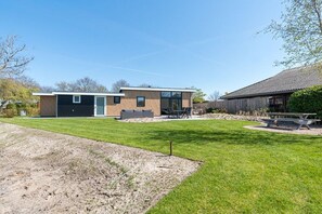 Ein modernes Haus mit einem gepflegten Rasen, einer Terrasse mit Gartenmöbeln und einem hölzernen Schuppen.