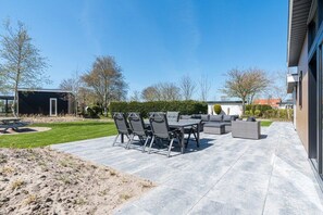 Ein Außenbereich mit einer Terrasse, einem Esstisch, Stühlen, einer Couch und einem kleinen Garten.