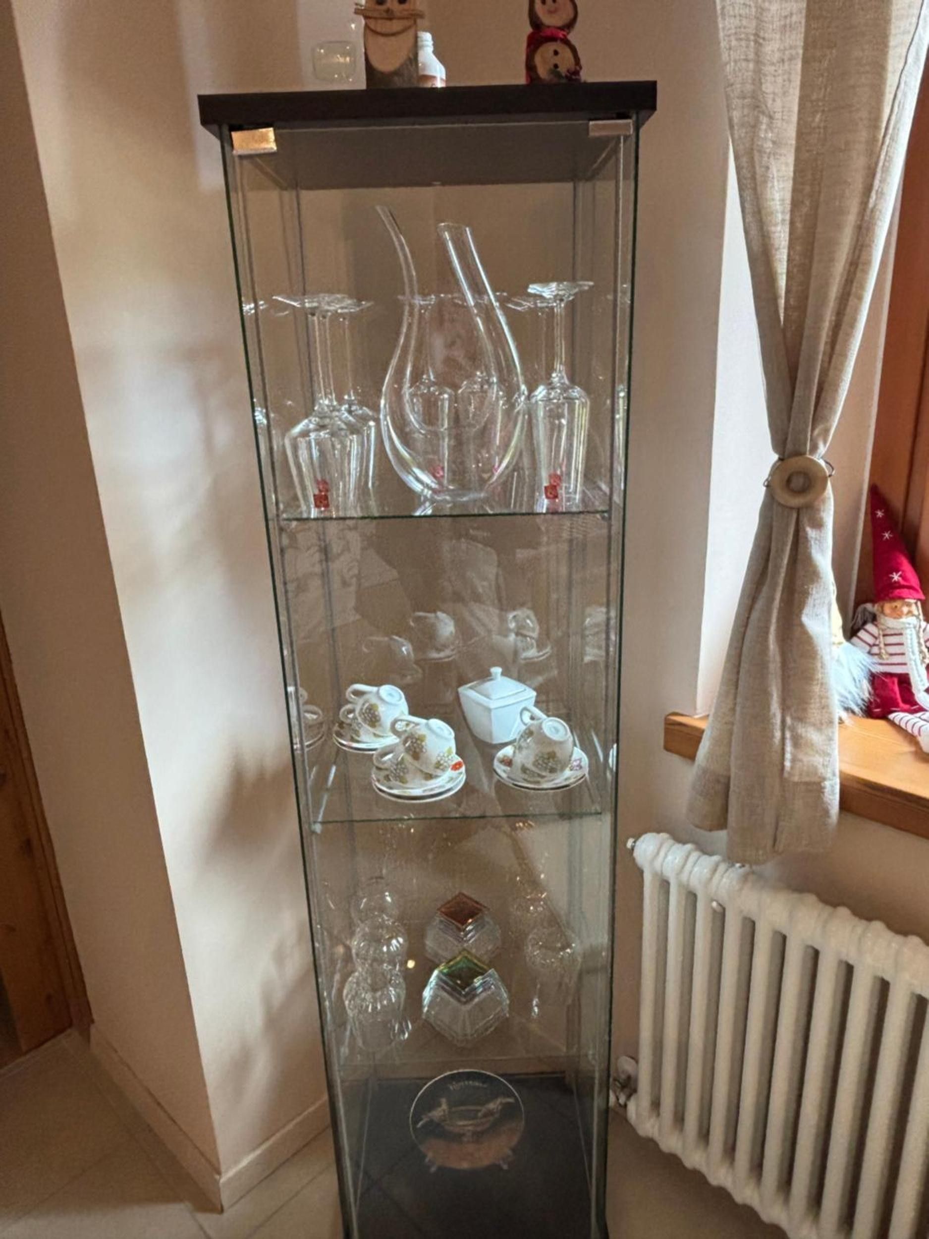 Un mueble vitrina alto de vidrio con diferentes vasos y vajinas de té de porcelana.
