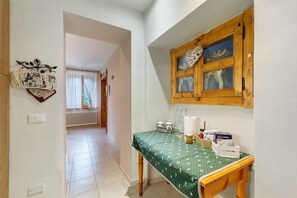 Une cuisine avec une table en bois, une fenêtre agrémentée d’un objet décoratif et un couloir menant à une autre pièce.