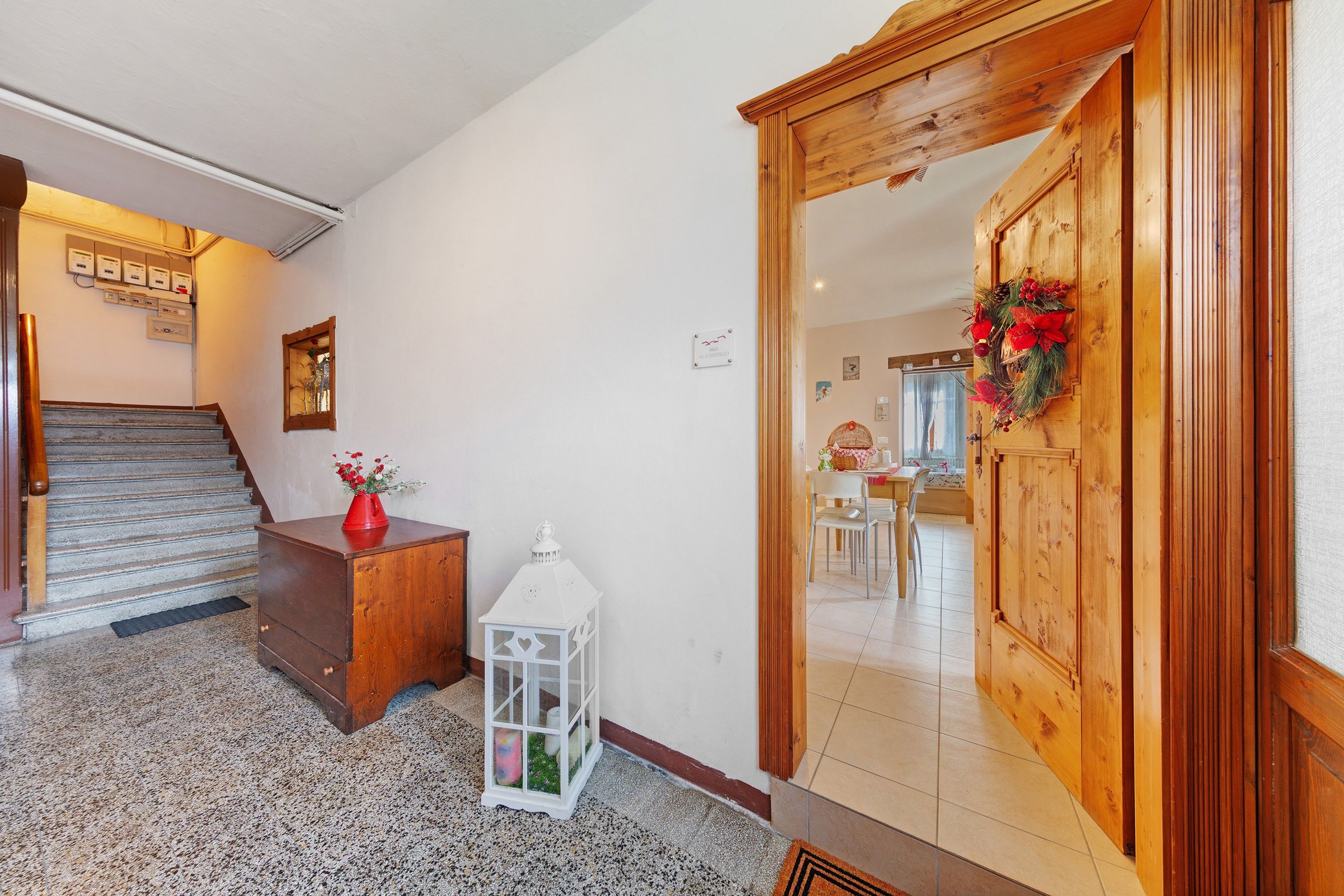 Un couloir avec une porte en bois, une petite table sur laquelle est posé un vase, et un escalier.