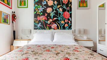 Un dormitorio con colcha estampada, dos mesitas de noche con lámparas y cuadros en las paredes.