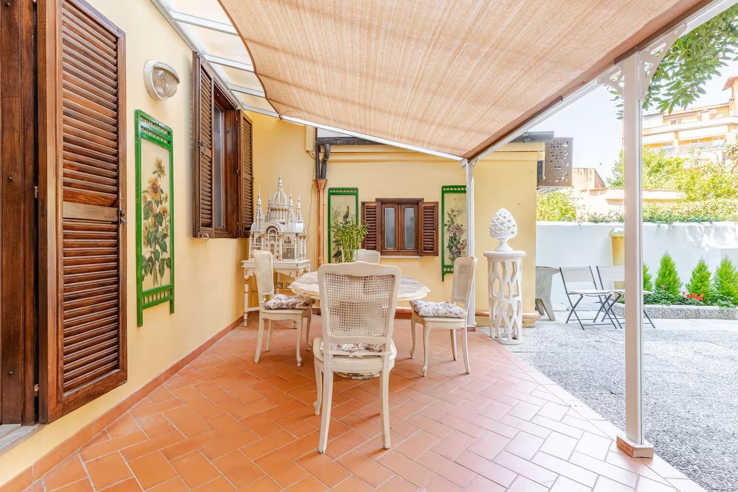 Un patio techado con una mesa y sillas, un comedero decorativo y vista a la calle.