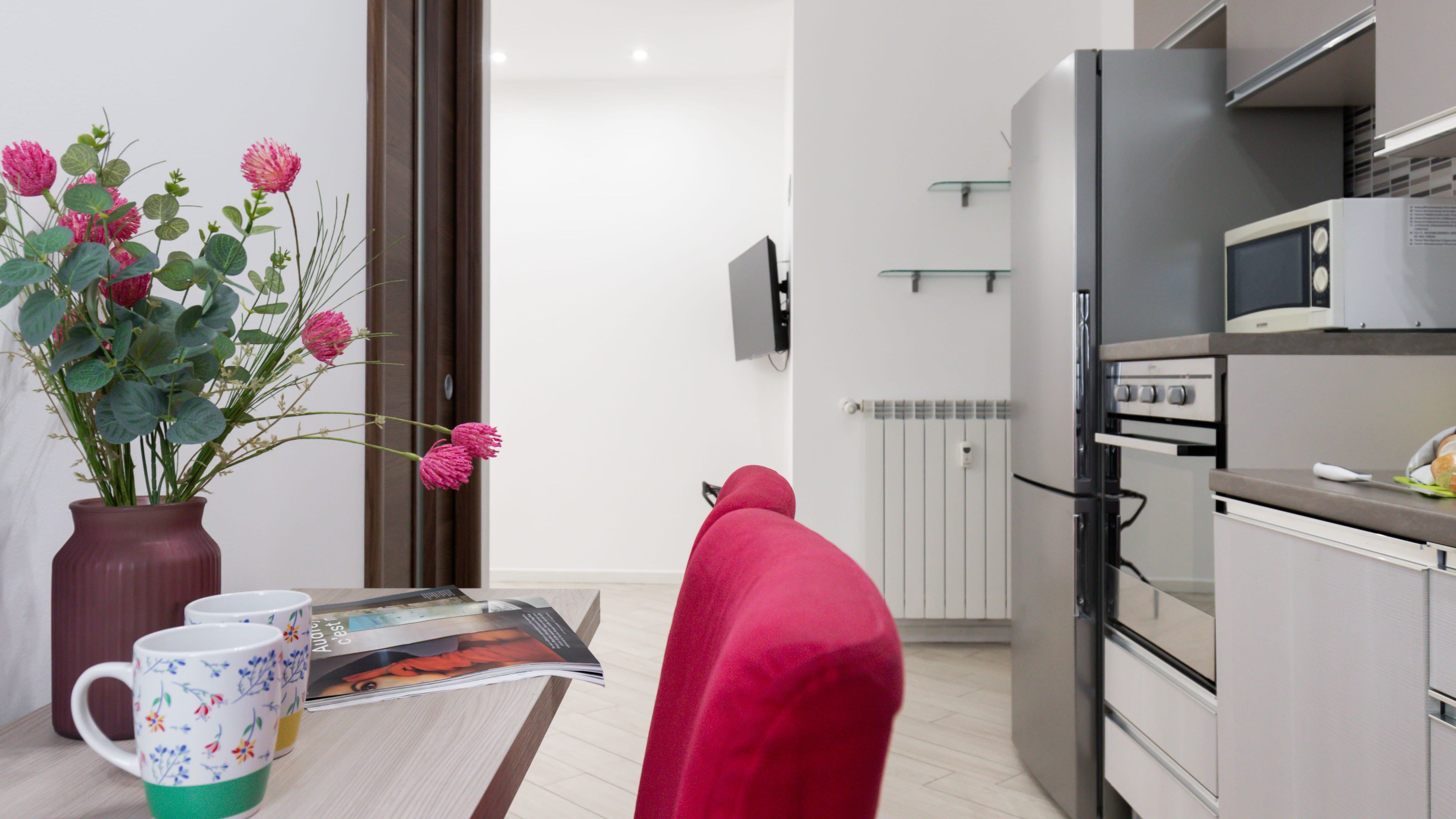 Una cocina moderna con refrigerador, microondas y horno. Hay un florero con flores en la encimera y una revista.