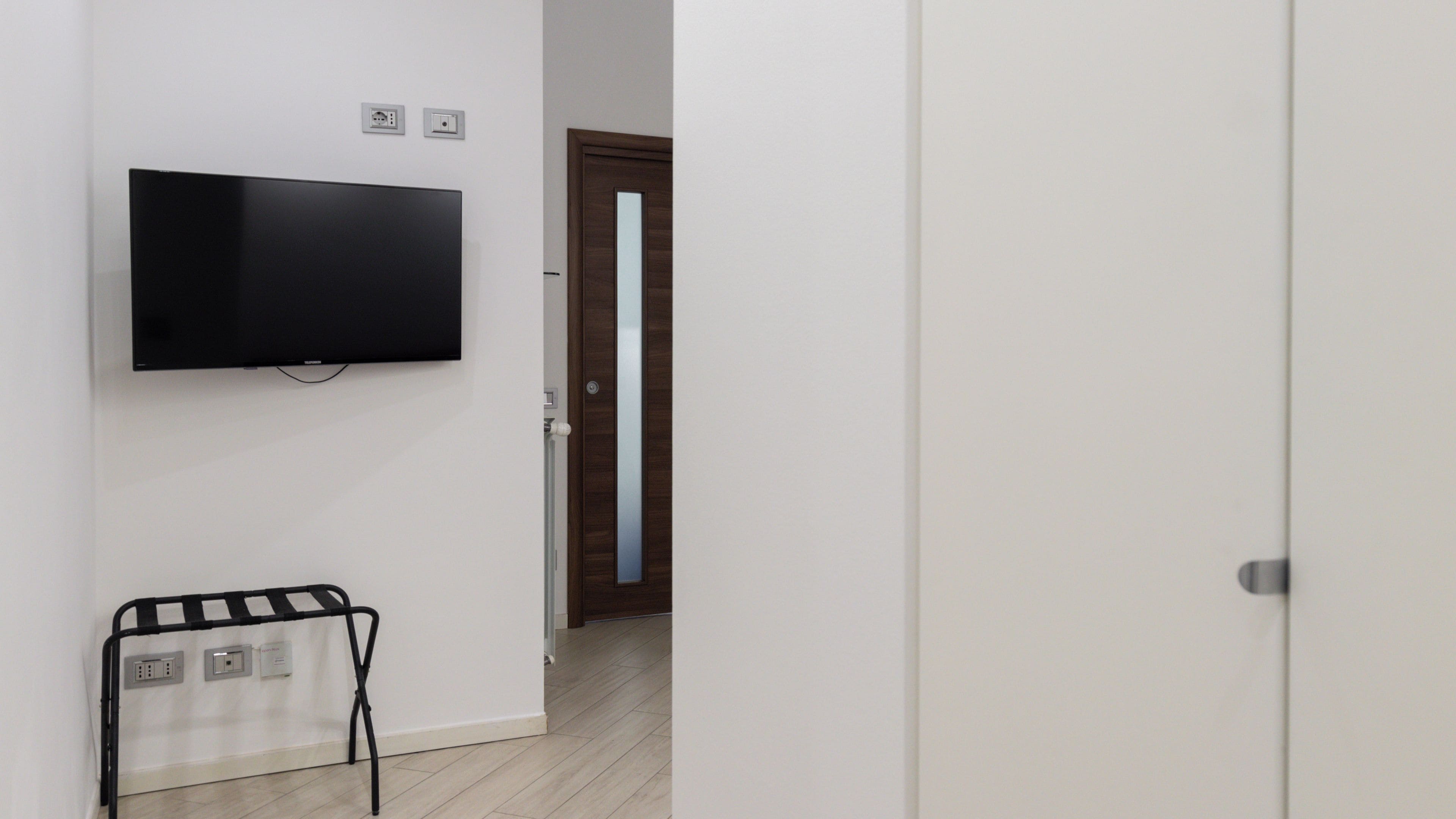 Una habitación con una televisión de pantalla plana montada en la pared, un radiador y una puerta que da a otra habitación.