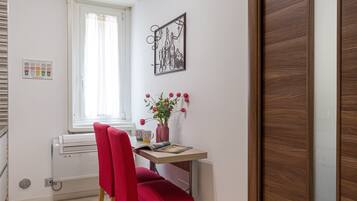 A room with a window, a radiator, a desk with a vase of flowers, a red chair, and a wooden door.