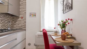 Une cuisine au design moderne, équipée d’une cuisinière à gaz, d’un four à micro-ondes et d’un four encastré. Une fenêtre offre une vue sur l’extérieur, et une petite table est agrémentée d’un vase de fleurs et d’un croissant.