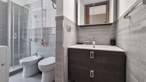 Une salle de bain moderne avec une douche à l’italienne en verre, un lavabo blanc et un meuble-lavabo en bois foncé.