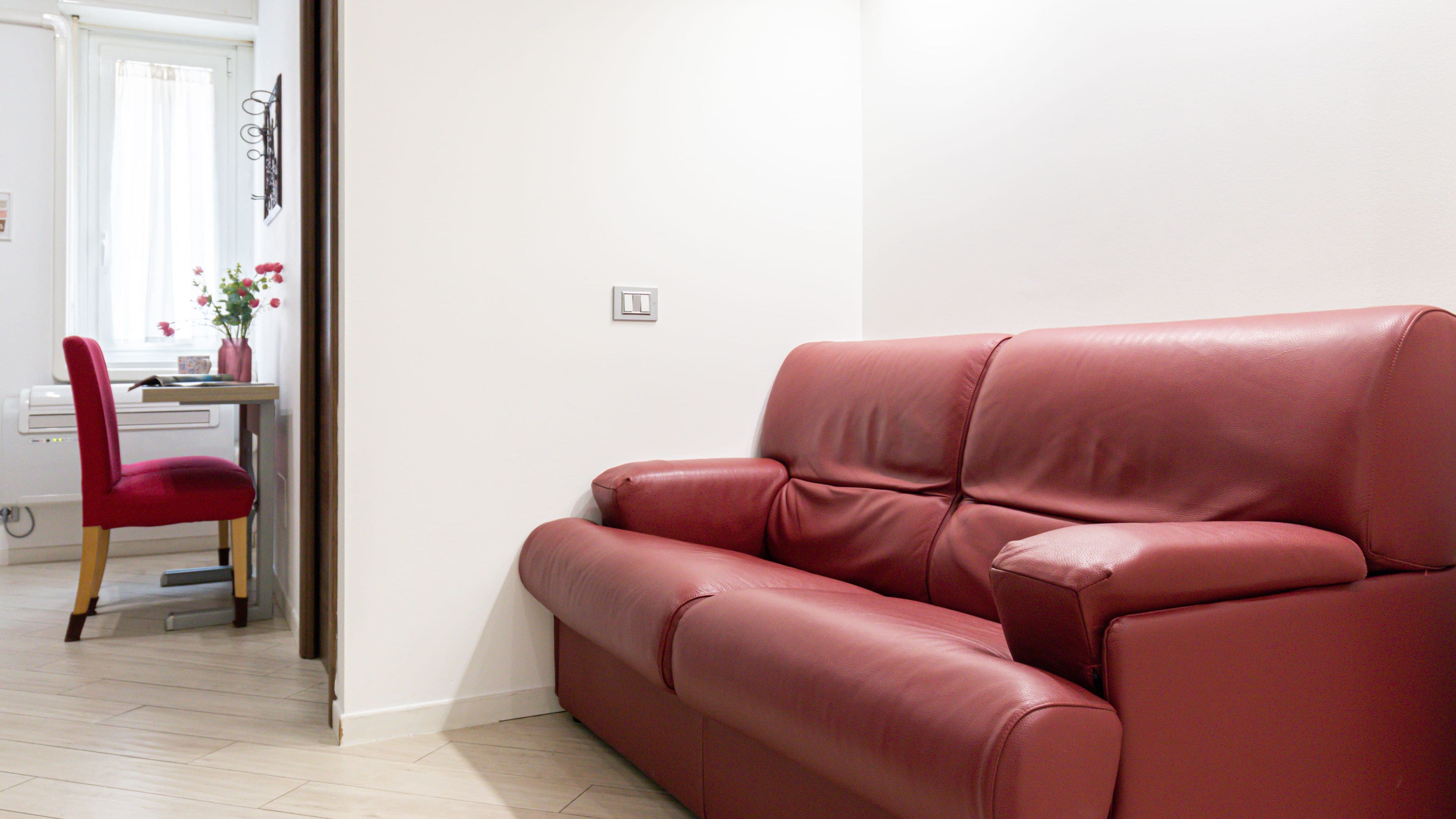 Un sofá de cuero rojo en una habitación con pared blanca y piso de madera.