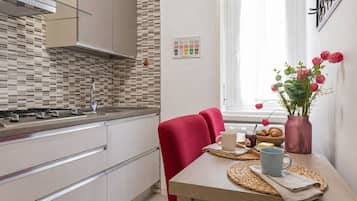 A modern kitchen with a tiled backsplash, a dining area with a red chair, and a table set with breakfast items.