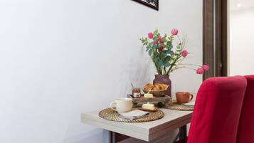 A breakfast setup with a vase of flowers, a jar of honey, croissants, and a cup on a wooden table.