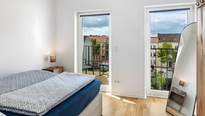 A bedroom with a bed, a nightstand, a window, and a view of the outside. - Apartment 'Elbe Panorama View' with Balcony, Wi-Fi and Air Conditioning (Wittenberge)