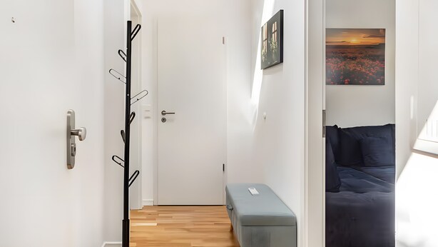 A hallway leading to a bedroom with a bed, a bench, and a coat rack. - Apartment 'Elbe Panorama View' with Balcony, Wi-Fi and Air Conditioning (Wittenberge)