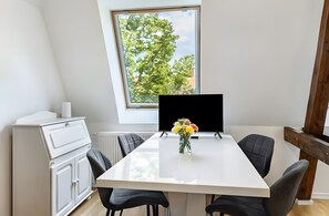 Et moderne spiseområde med et hvidt bord, sorte stole, en vase med blomster og et vindue med udsigt til træer.