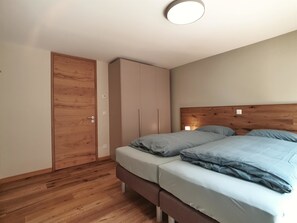Ein Schlafzimmer mit Holzboden, einem Bett mit grauer Bettwäsche, einem hölzernen Kopfteil und einem Kleiderschrank.